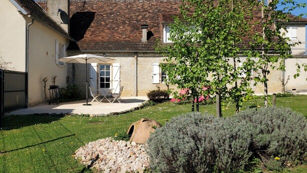 Une cour avec un mur en pierre, un arbre, un petit jardin et une porte blanche.