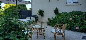 A patio with wicker furniture, a table, and chairs, surrounded by greenery and a building with windows. - Completely renovated 4-person gîte in the countryside, north of the Lot. (Cavagnac)