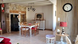 Un salon chaleureux avec un canapé rouge, un coin repas avec des chaises en bois, un mur en pierre et une cheminée.