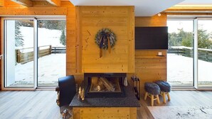 A modern interior with a fireplace, wooden walls, and large windows offering a view of a snowy outdoor area. - Chalet At Le Petit Paradis – Hot Tub, Sauna and Gym (Gérardmer)