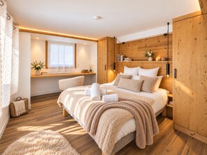 A modern bedroom with a large bed, wooden paneling, a window with lace curtains, and a bedside table with books and candles. - Chalet At Le Petit Paradis – Hot Tub, Sauna and Gym (Gérardmer)