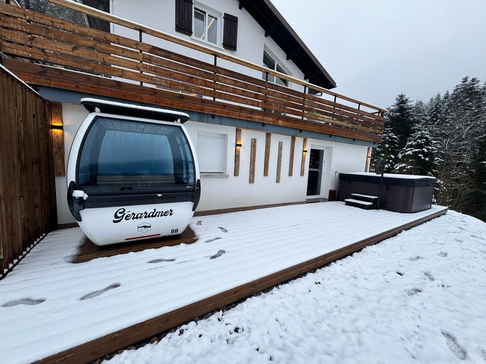 Una terrassa coberta de neu amb un teleàsics i una banyera d'hidromassatge.