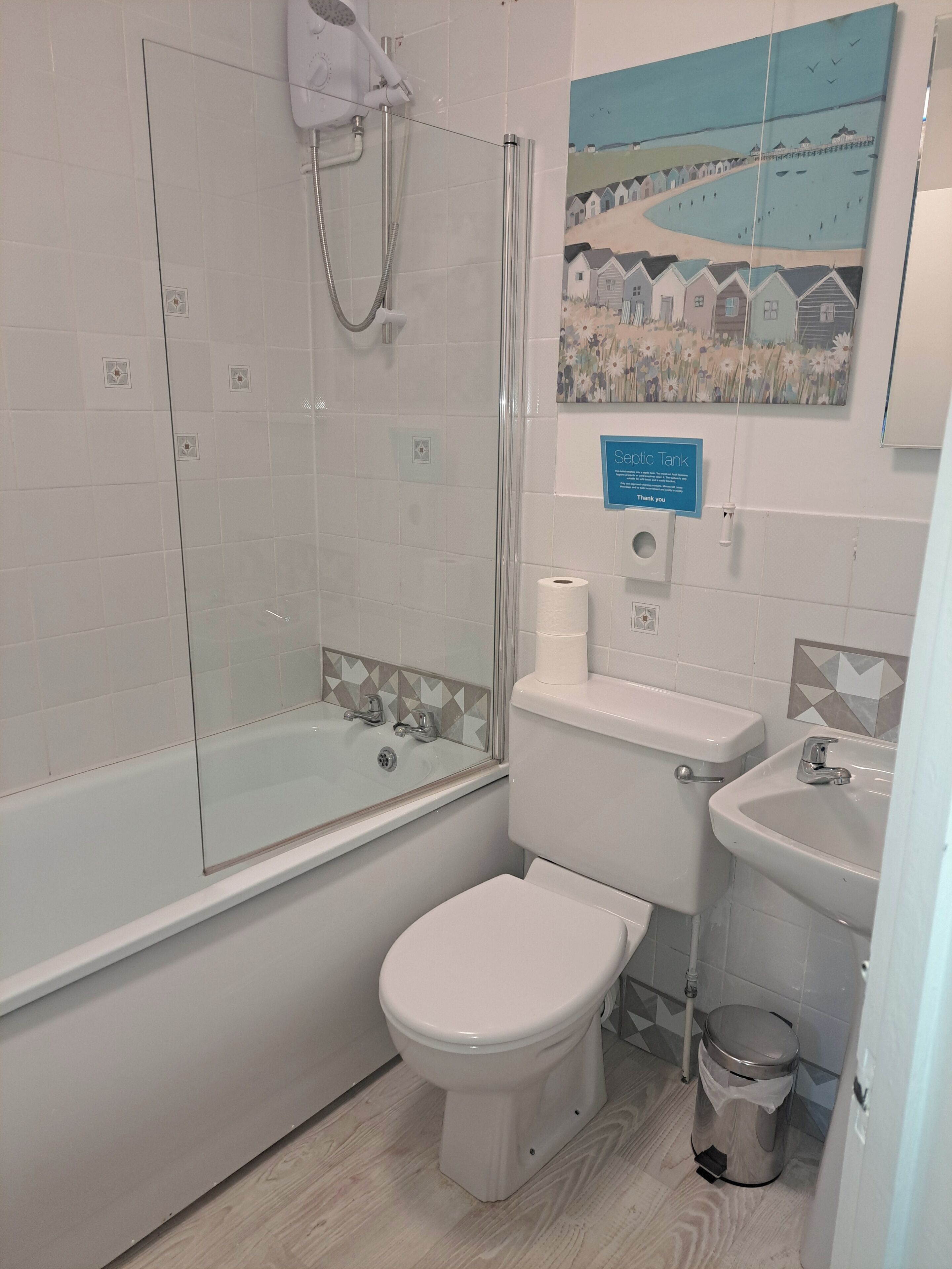 Een badkamer met een douchecabine van glas, een toilet, een wastafel en een prullenbak.