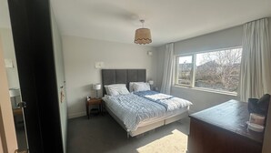 A bedroom with a bed, bedside tables, a lamp, a window with curtains, and a view of the outside. - Bright Spacious 5-bedroom house in Dundrum with sunken Trampoline and Treehouse. (Dublin 8)