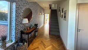 A hallway with patterned wallpaper, a round mirror, a lamp, a staircase, and framed pictures on the wall. - Bright Spacious 5-bedroom house in Dundrum with sunken Trampoline and Treehouse. (Dublin 8)