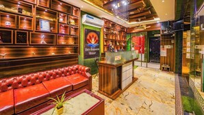 A hotel lobby with a red leather sofa, wooden shelves with framed items, a reception desk, and a sign for 'Shiv Roodrayaam Retreat'. - Shiv Rudraksh Resort - Near Assi Ghat (Varanasi)