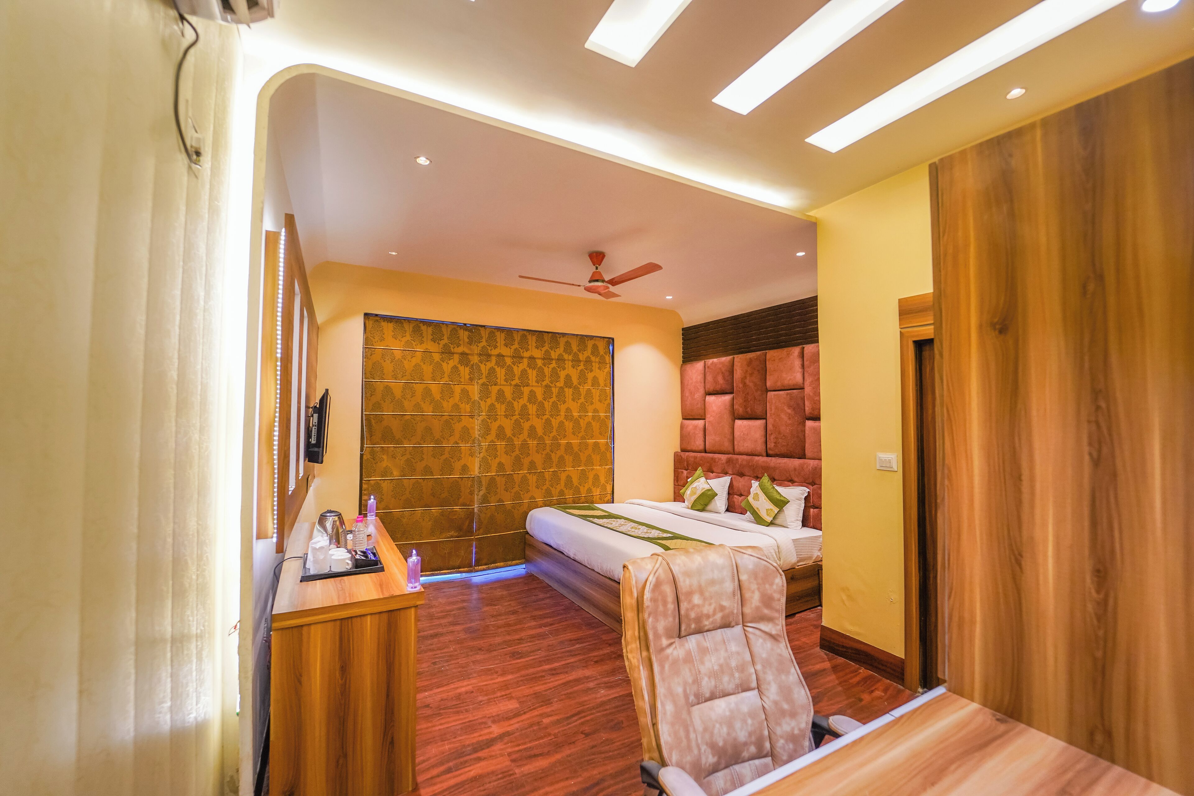 Quarto de hotel moderno com cama, escrivaninha, cadeira e ventoinha no teto.