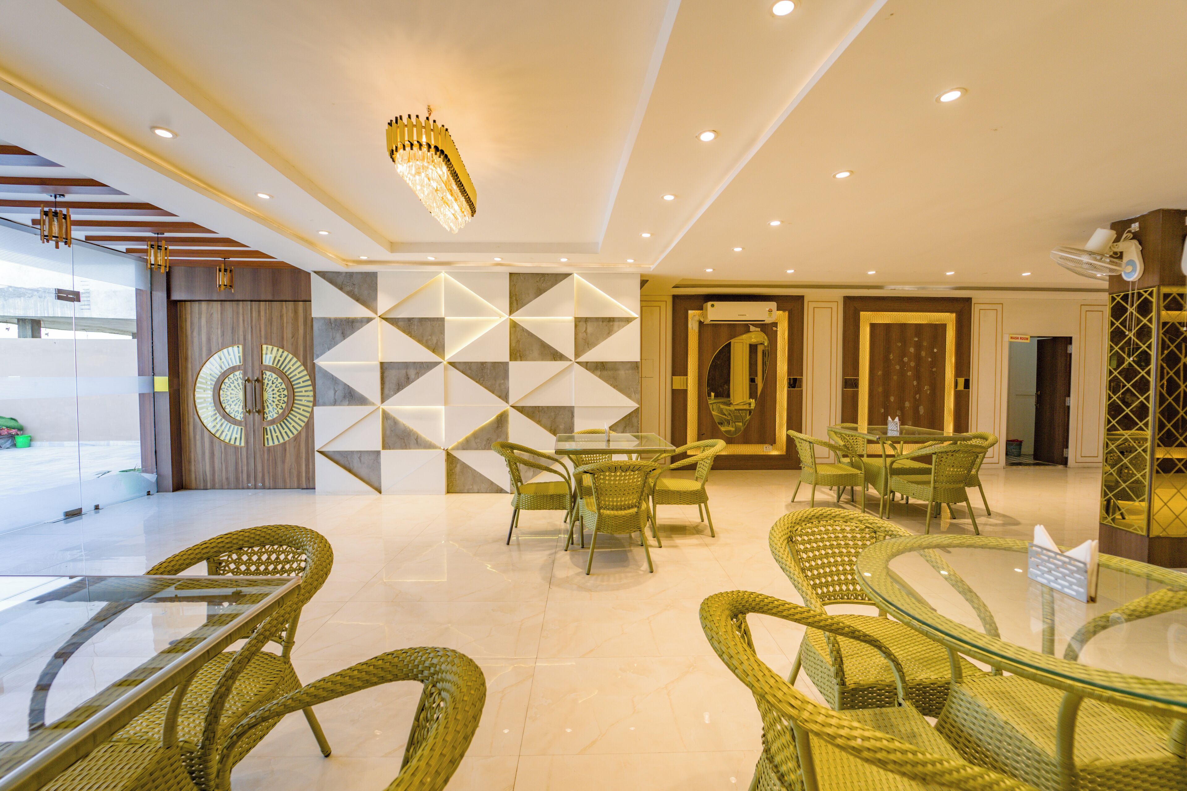 Een moderne hotellobby met een glazen tafel, rieten stoelen en een geometrisch wandontwerp.