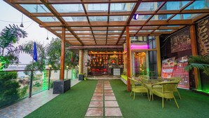 Un área de estar al aire libre techada con césped artificial, un sendero de piedra, mobiliario de mimbre y vistas al restaurante interior.