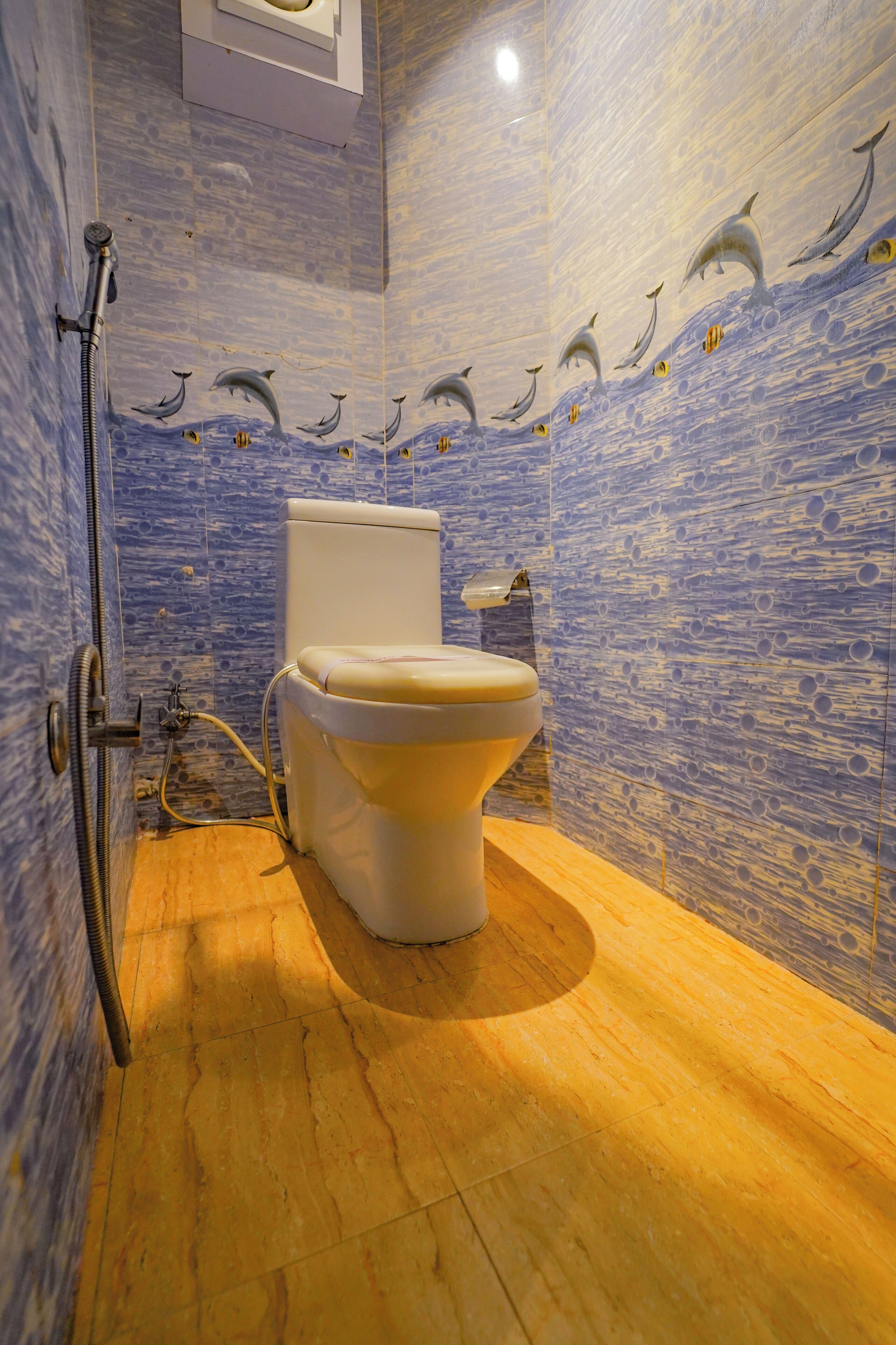 Een badkamer met toilet, douche en betegelde muren met motieven van dolfijnen en golven.