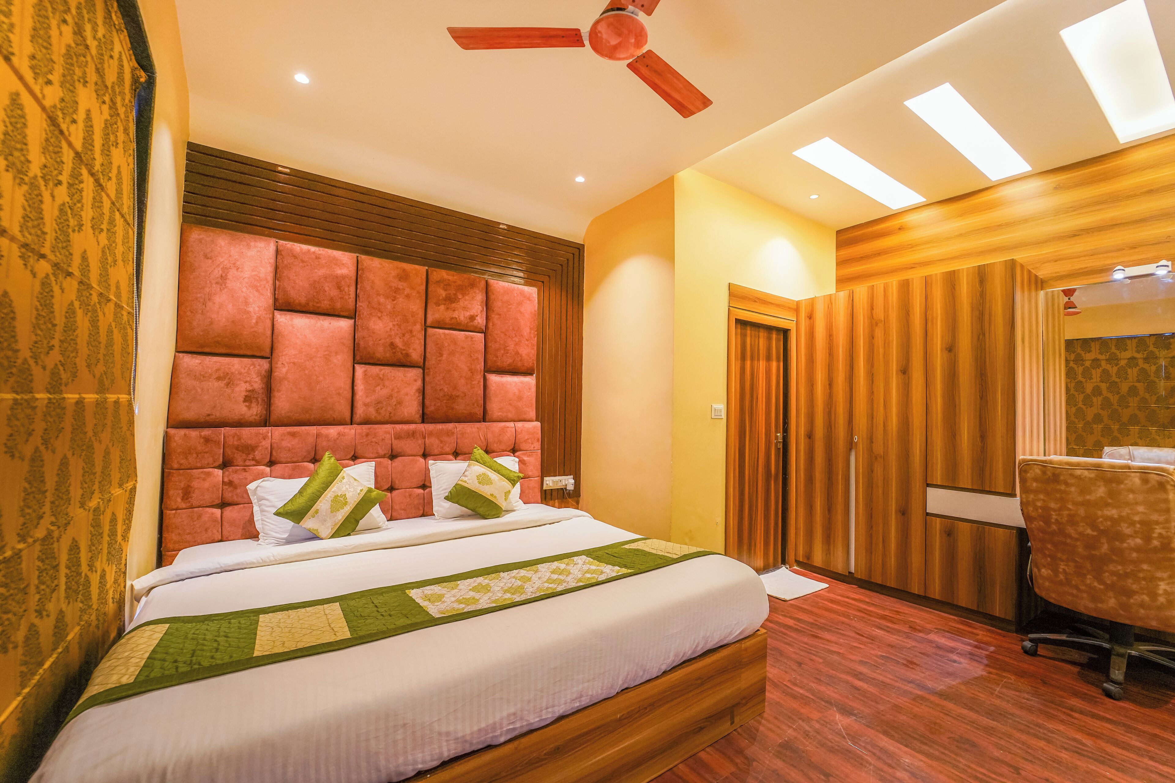 Una habitación de hotel con una cama grande, un cabecero de madera, un ventilador de techo y un escritorio con una silla.