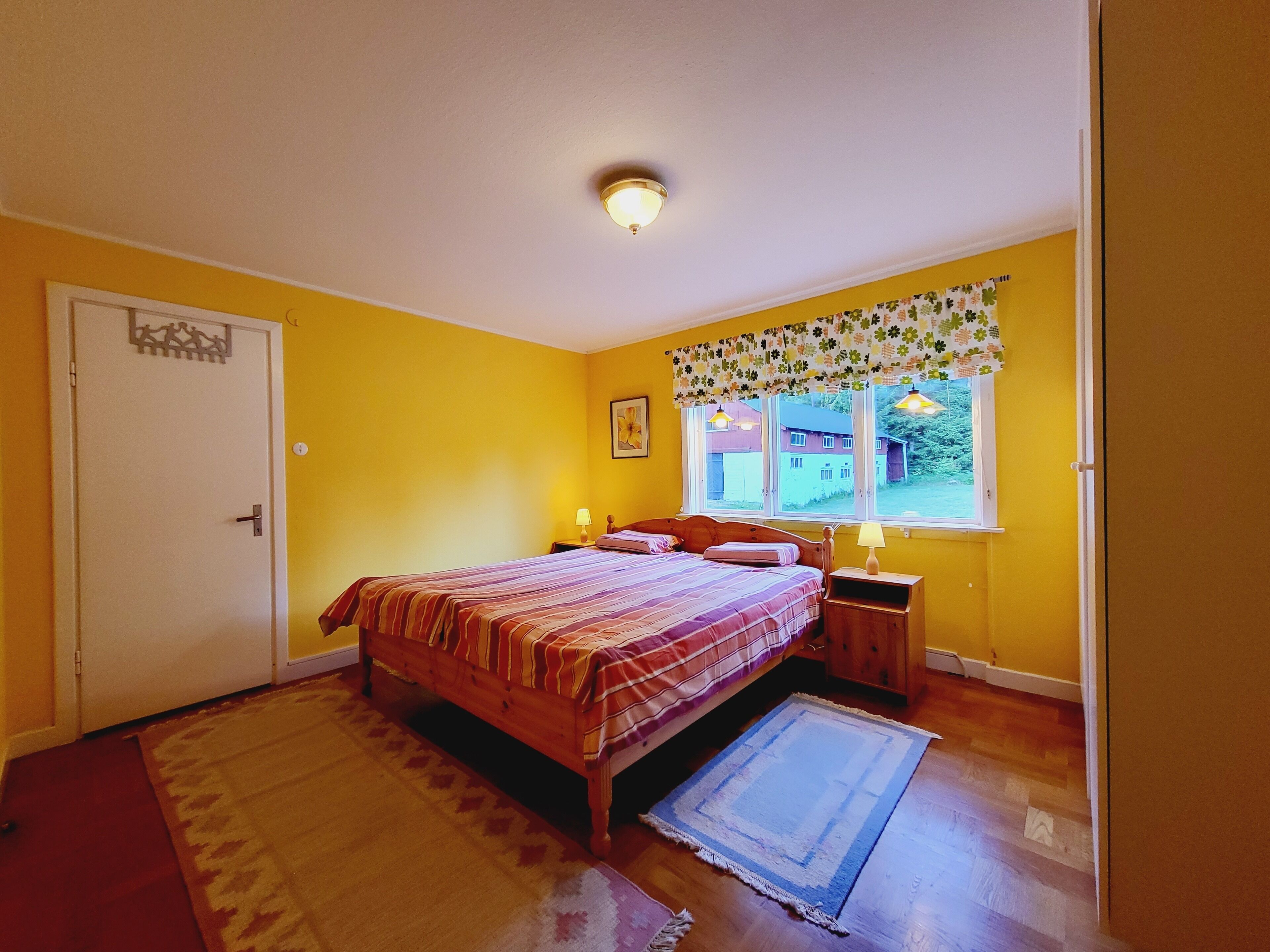 A bedroom with a bed, bedside tables, a window with curtains, a door, and a patterned rug.