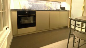 A modern kitchen with a built-in oven, a countertop with a coffee maker, and a dining area with a chair.