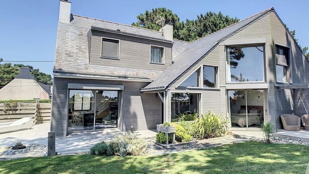 Une maison moderne à deux étages, dotée d’un toit en pente, de grandes fenêtres et d’un patio couvert.