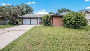 A residential house with a garage, a well-maintained lawn, and a large evergreen tree.