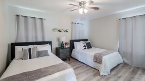A hotel room with two beds, a ceiling fan, and a nightstand with a lamp and flowers.