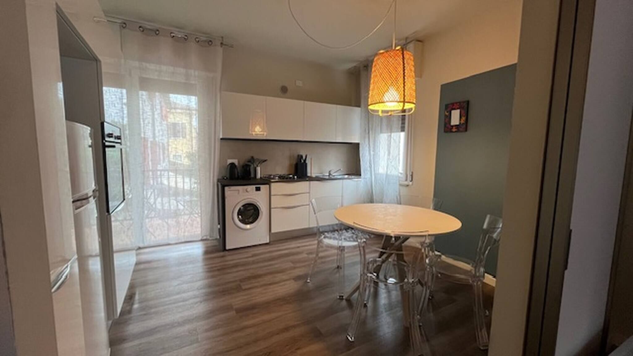A compact kitchen with a washing machine, a dining table with chairs, and a hanging light fixture.
