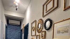 Un pasillo con piso de madera, una lámpara en el techo y una pared decorada con varios marcos.