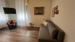 Una sala de estar con un sofá, un sillón colorido, una mesita y un cuadro en la pared.