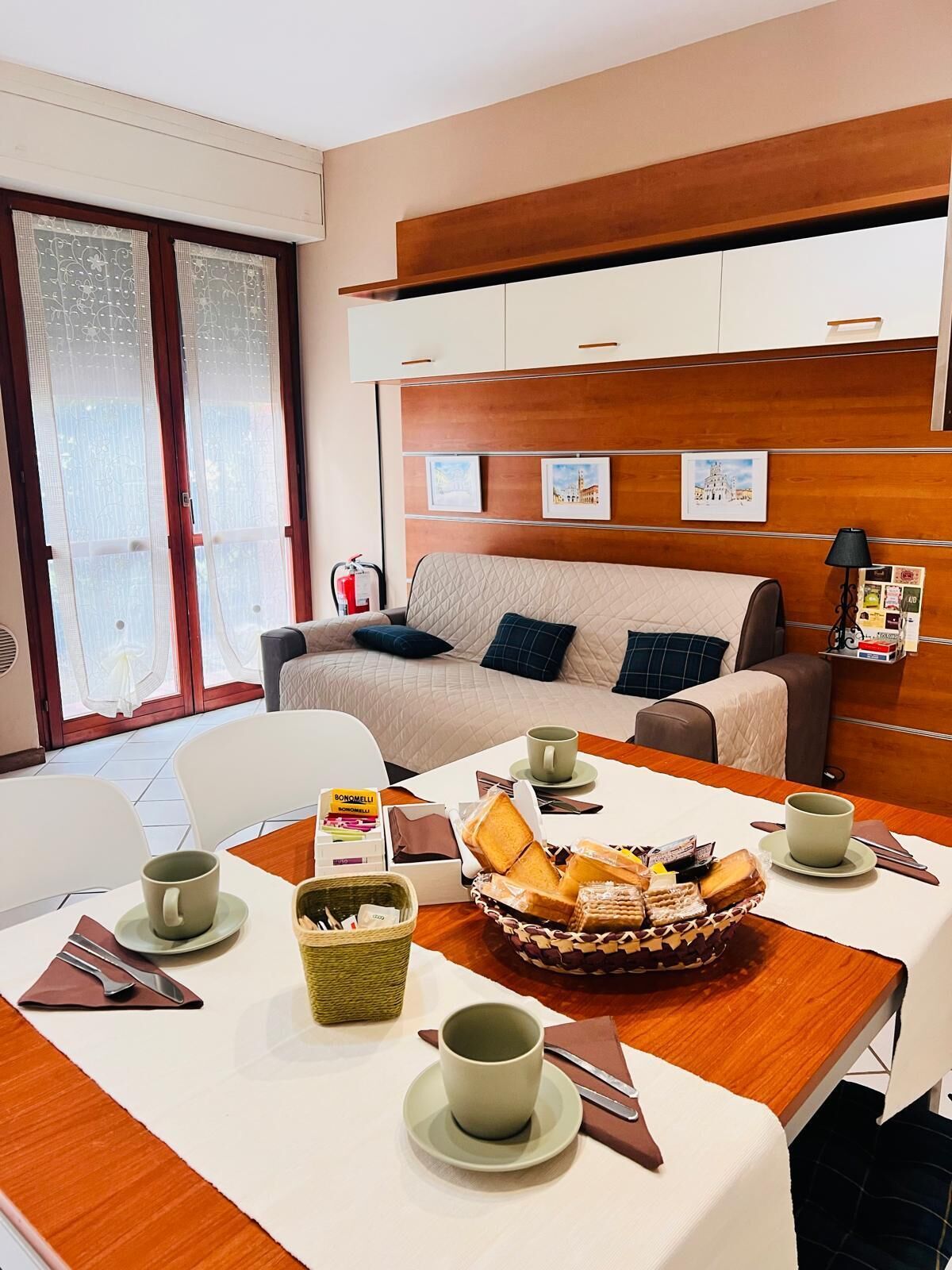 A hotel room with a dining area, a sofa, and a bed. There are pictures on the wall and a basket of food on the table.