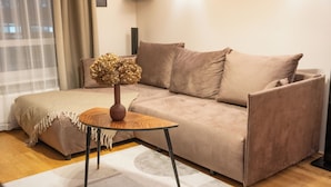 A living room with a beige sofa, a small wooden side table with a vase, and a patterned rug.