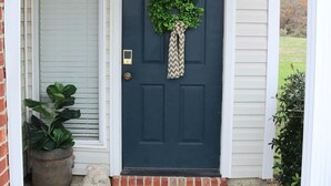 A dark blue front door with a wreath and a chevron-patterned curtain, a potted plant, and a stone lion statue on the porch. - The Grace at the Highlands - Charming 2-bedroom townhome close to MSU campus (Starkville)