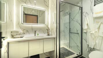 Un baño moderno con detalles de mármol en el salpicadero, una cabina de ducha de cristal y un tocador con espejo y toallero.