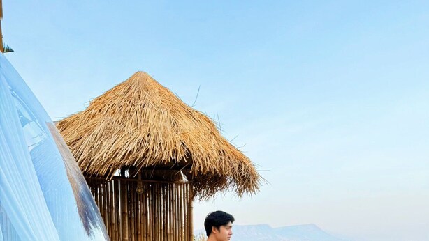A man standing on a wooden deck with a thatched-roof structure behind him, overlooking a landscape. - PARACH RESORT KHAOKHO (Khao Kho)
