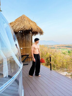 A man standing on a wooden deck with a thatched-roof structure behind him, overlooking a landscape. - PARACH RESORT KHAOKHO (Khao Kho)