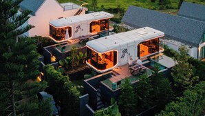A modern eco-friendly house with multiple rooms, large glass windows, and a view of wind turbines in the background. - PARACH RESORT KHAOKHO (Khao Kho)