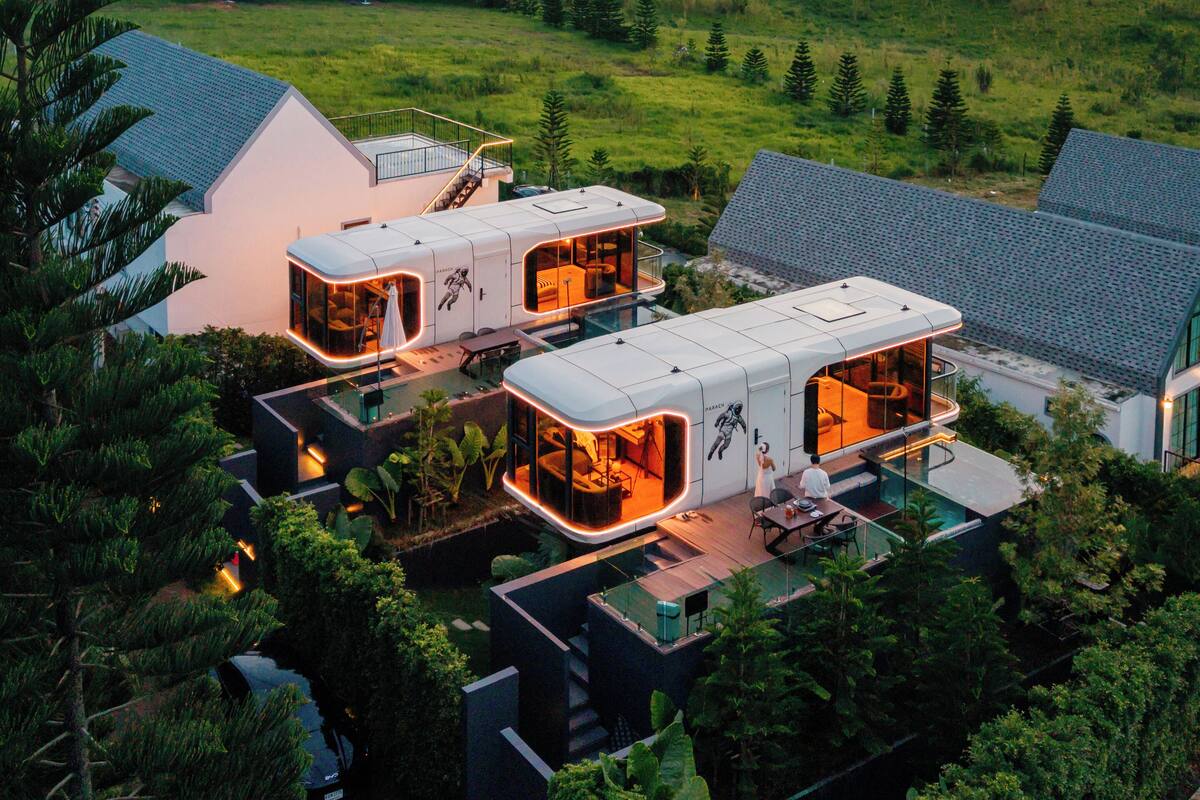 A modern eco-friendly house with multiple rooms, large glass windows, and a view of wind turbines in the background.