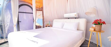 A bedroom with a bed, a bedside table, a lamp, and a window.
