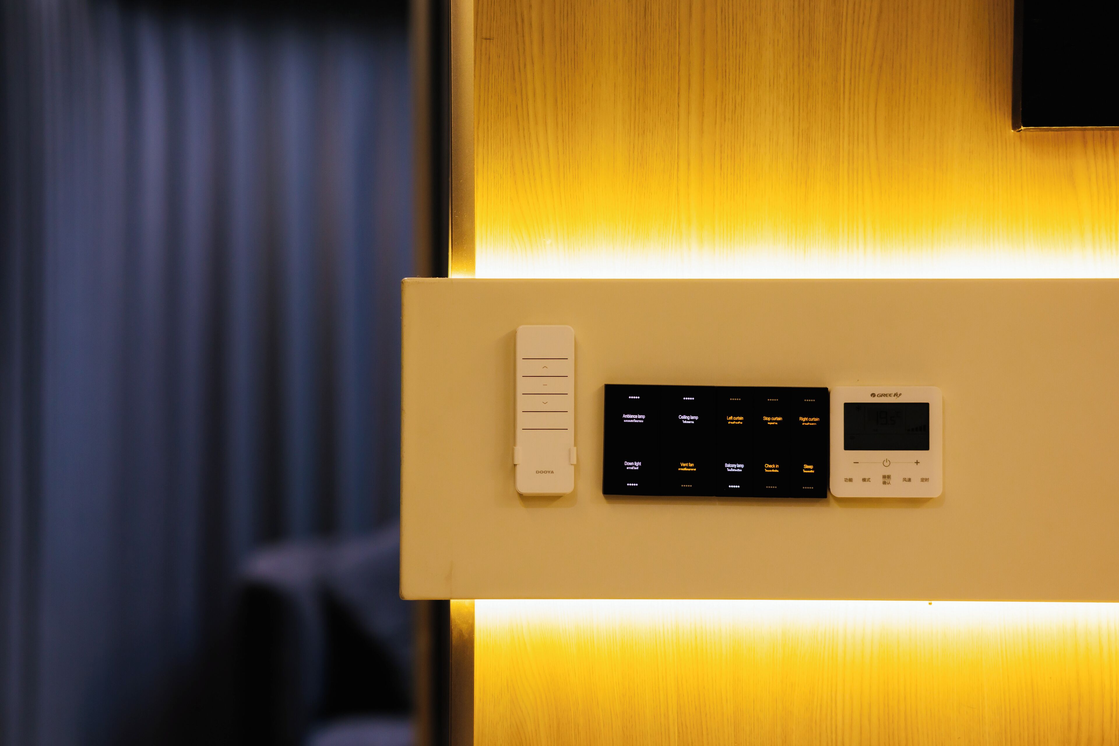 A control panel with a thermostat and a digital display, likely for room temperature control, mounted on a wall with a wooden finish.