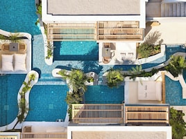 An aerial view of a resort with multiple swimming pools, wooden deck areas, and lush greenery.