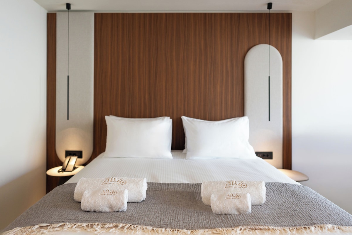 Una habitación de hotel moderna con una cama grande, dos mesitas de noche y un cabecero de madera.