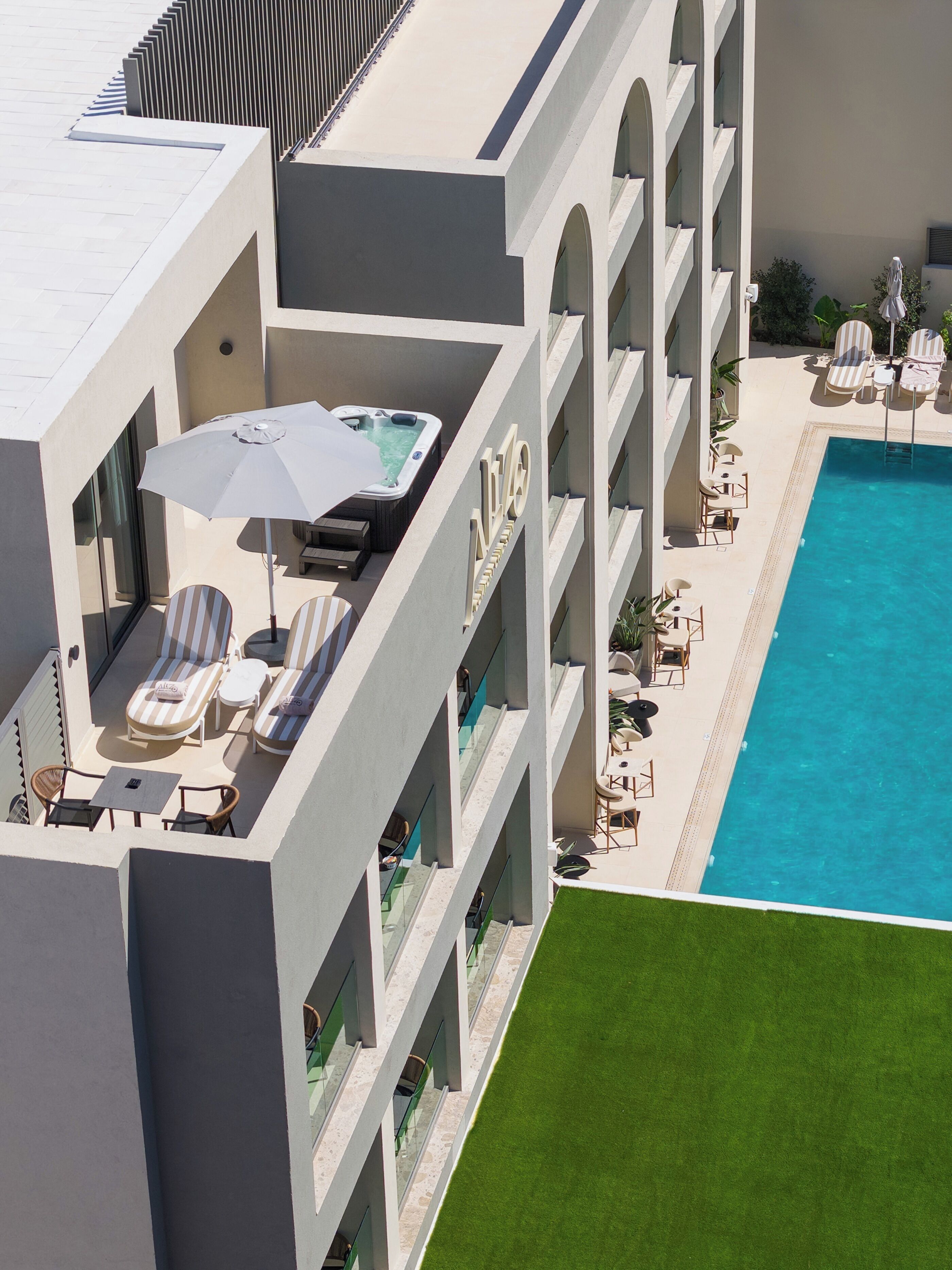 A modern hotel with a rooftop pool area, lounge chairs, and a hot tub.