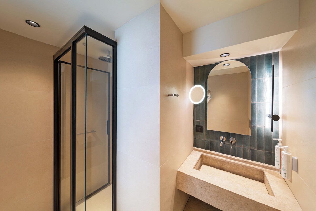 Un baño moderno con cabina de ducha de vidrio, lavamanos con espejo y aplique de pared.