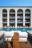 A pool area with lounge chairs and a wooden table, overlooking a building with multiple balconies.