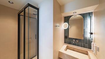 Un baño moderno con cabina de ducha de vidrio, lavamanos con espejo y aplique de pared.