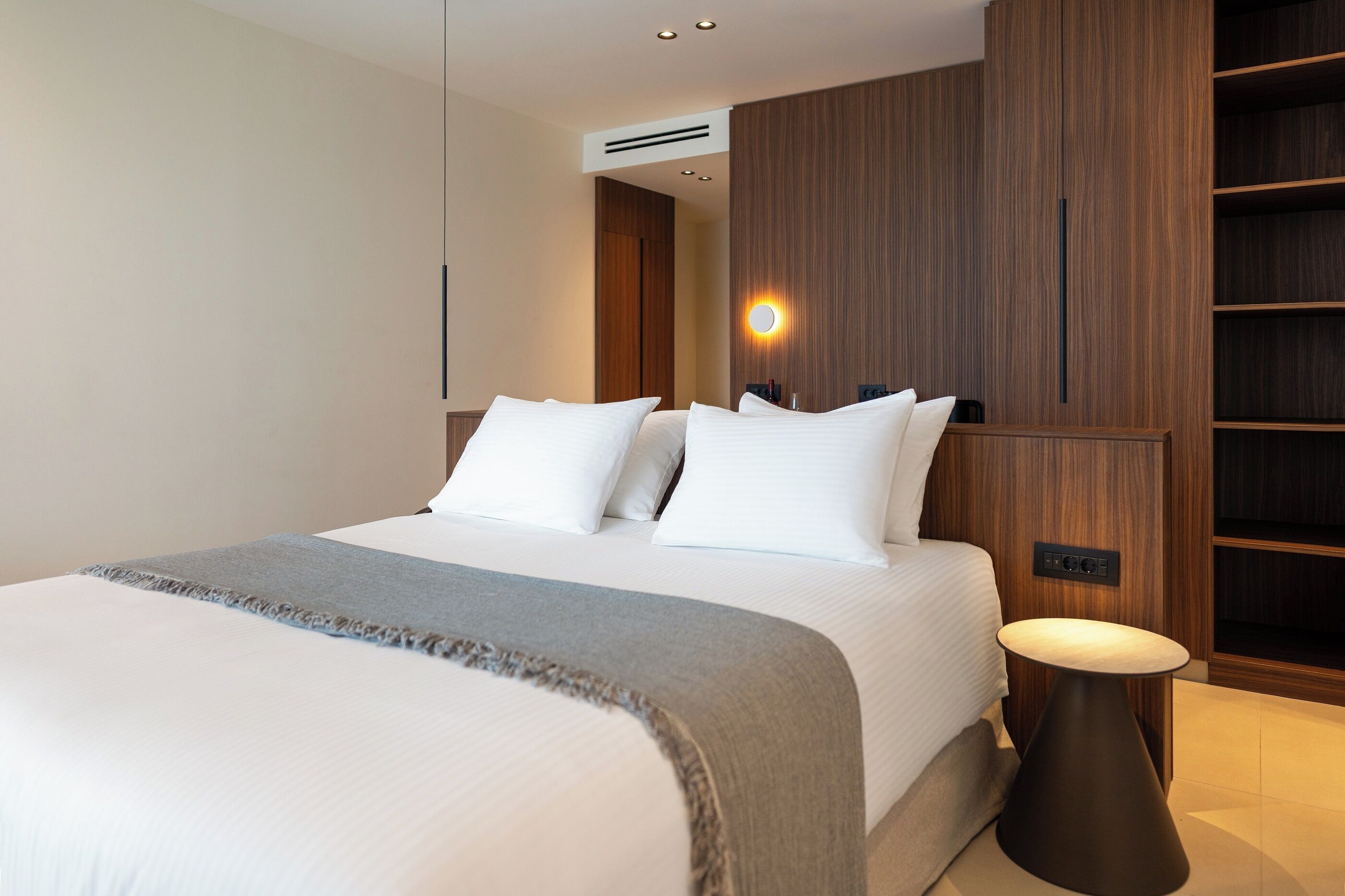Une chambre d’hôtel moderne avec un grand lit, une table de chevet et des étagères en bois intégrées.