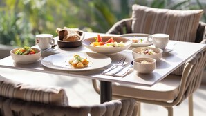 A dining table with various dishes, cups, and cutlery, set in a bright, sunlit room with a view of greenery outside.