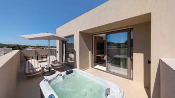 Terraza en la azotea con jacuzzi, sillones de descanso y puerta de vidrio que da a un espacio interior.