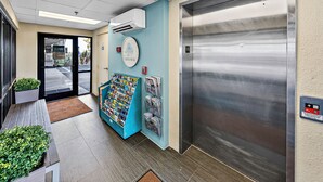 Un ascenseur aux finitions métalliques, une horloge murale et un présentoir à magazines contenant diverses publications.