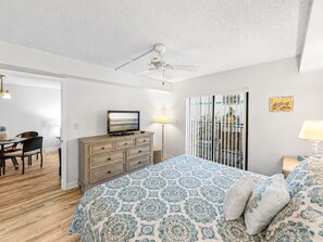 A bedroom with a bed, dresser, television, and a balcony view.