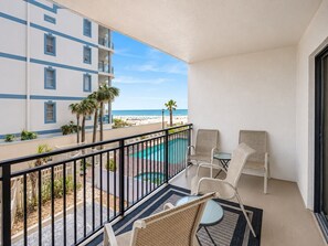 A balcony with a pool, chairs, and a view of the beach and ocean.