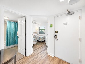 A room with a bed, a desk, and a door leading to another room.