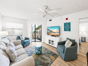 A living room with a sofa, armchair, TV, and a view of the outdoors through a sliding door.
