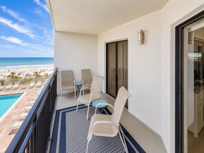 A balcony with a view of the beach, a pool, and a door to the room.