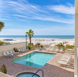 A pool area with lounge chairs and a view of the beach.