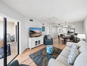A modern living room with a flat-screen TV, a sofa, a coffee table, and a dining area with a table and chairs.